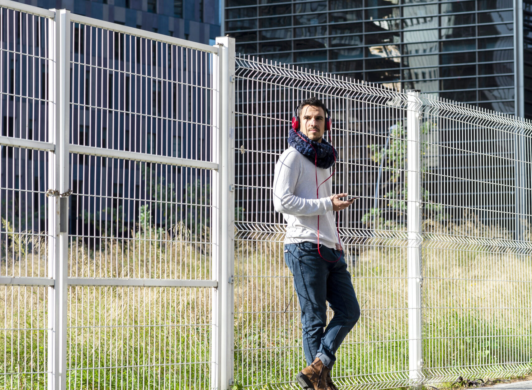 Young man listening music by headphones while holding a mobile phone outdoor